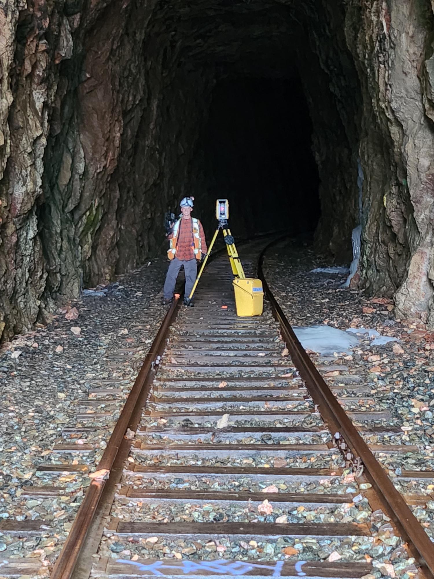 Instrument d’arpentage devant un tunnel ferroviaire.